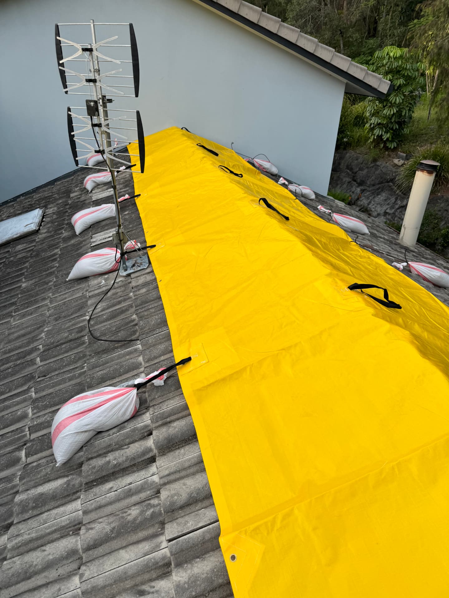 Yellow heavy-duty tarp run down a tiled roof plane and ballasted with sandbags on every strap