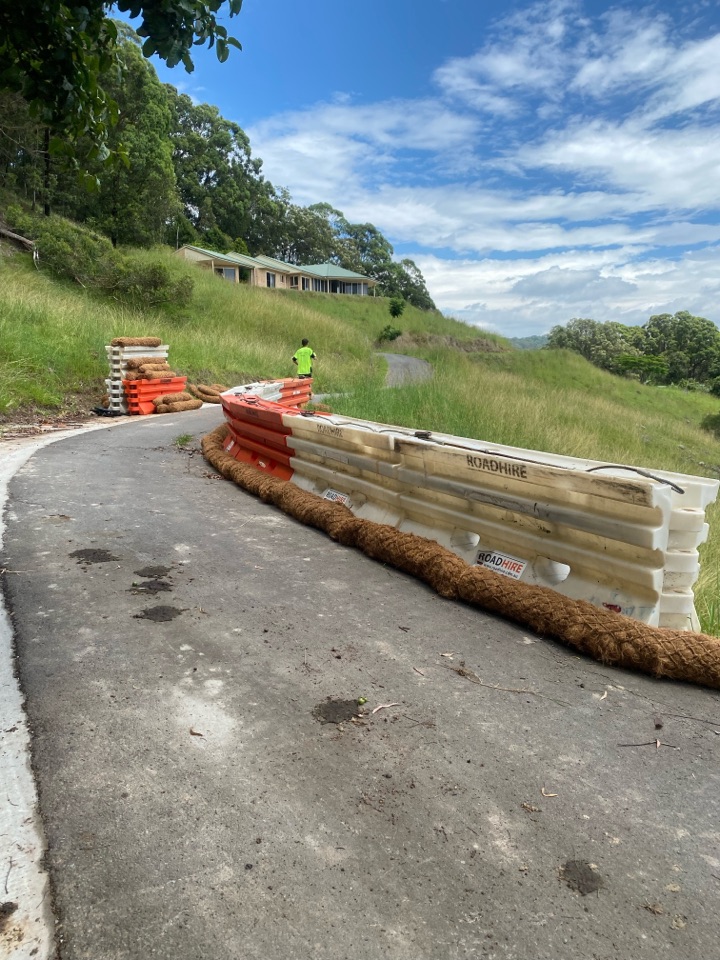 Water-filled road barriers and coir logs closing off a damaged section of access road