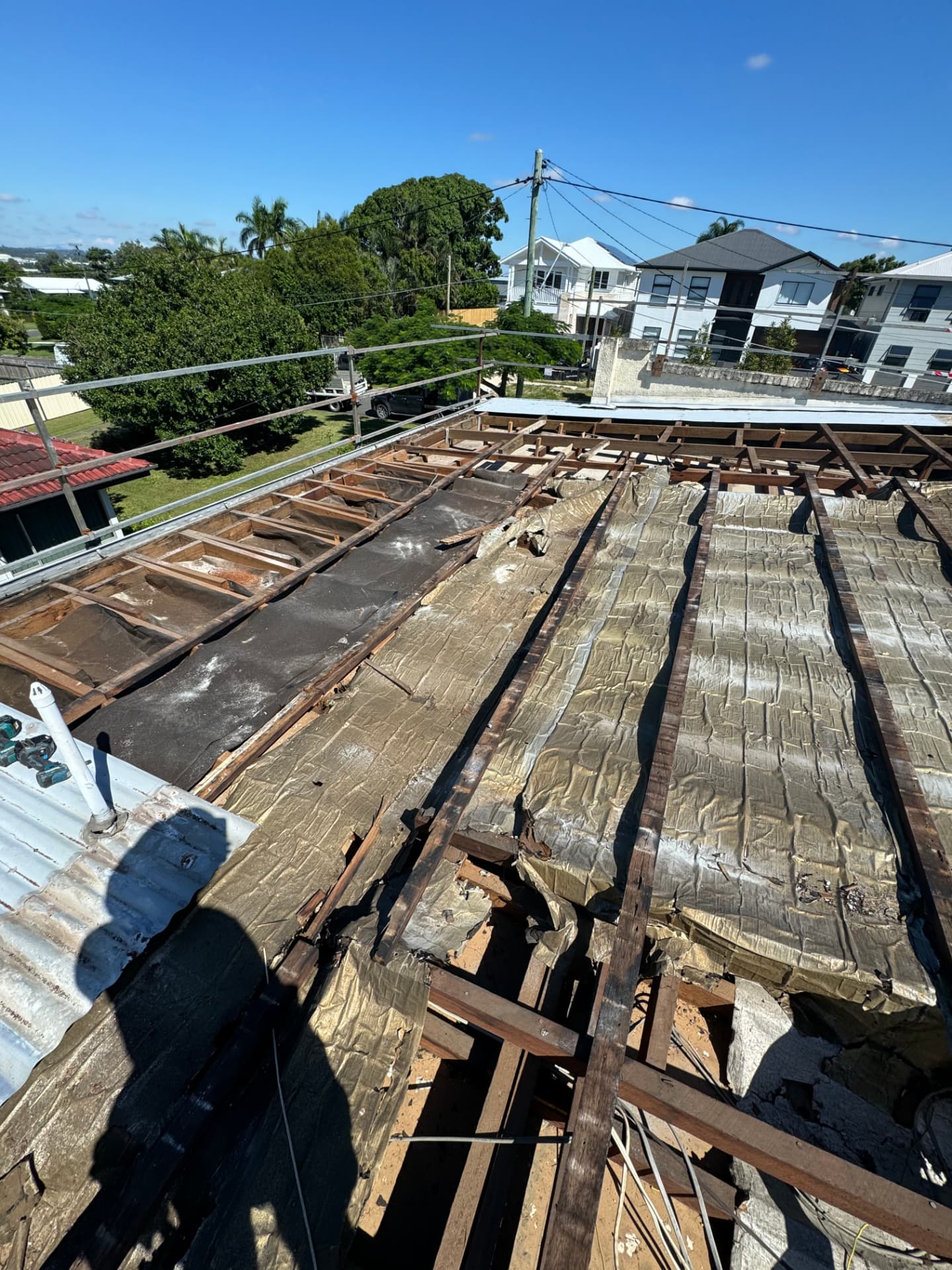 Storm-damaged roof opened up to exposed framing and torn sarking, with edge protection installed around the perimeter