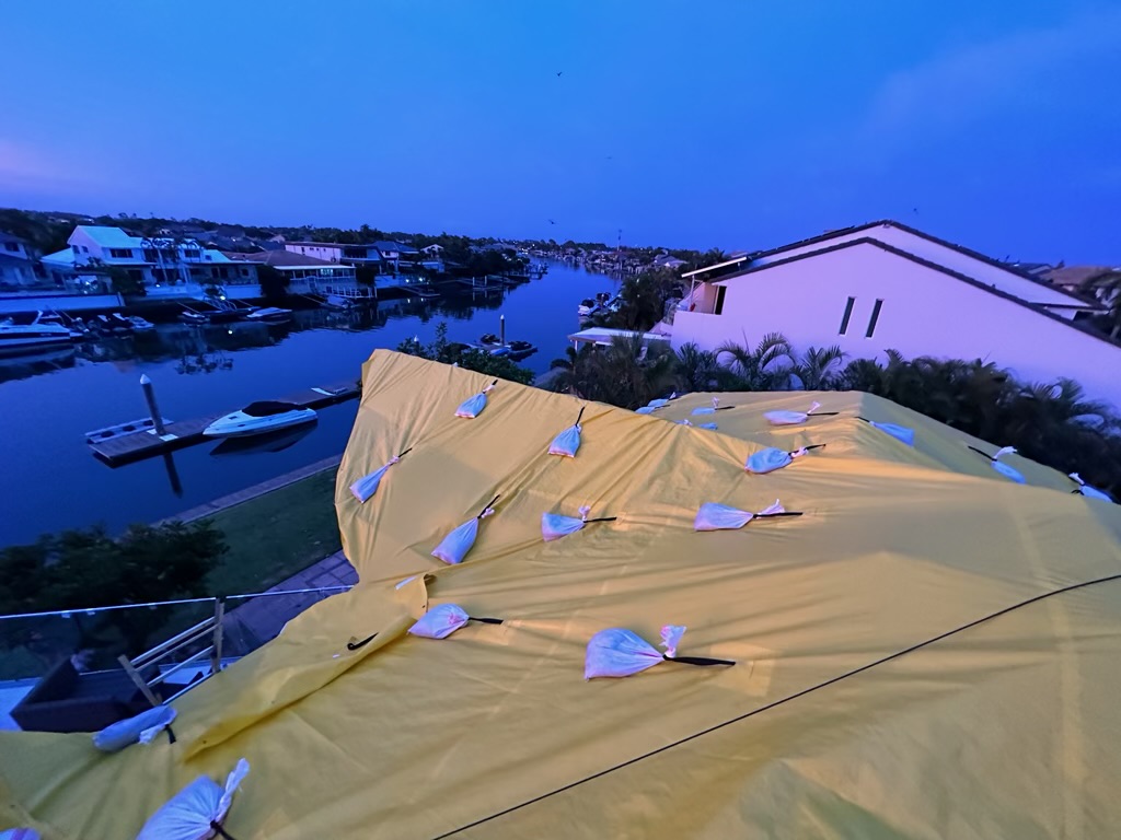 Temporary roof cover strapped and sandbagged over a canal-front roof during blue hour