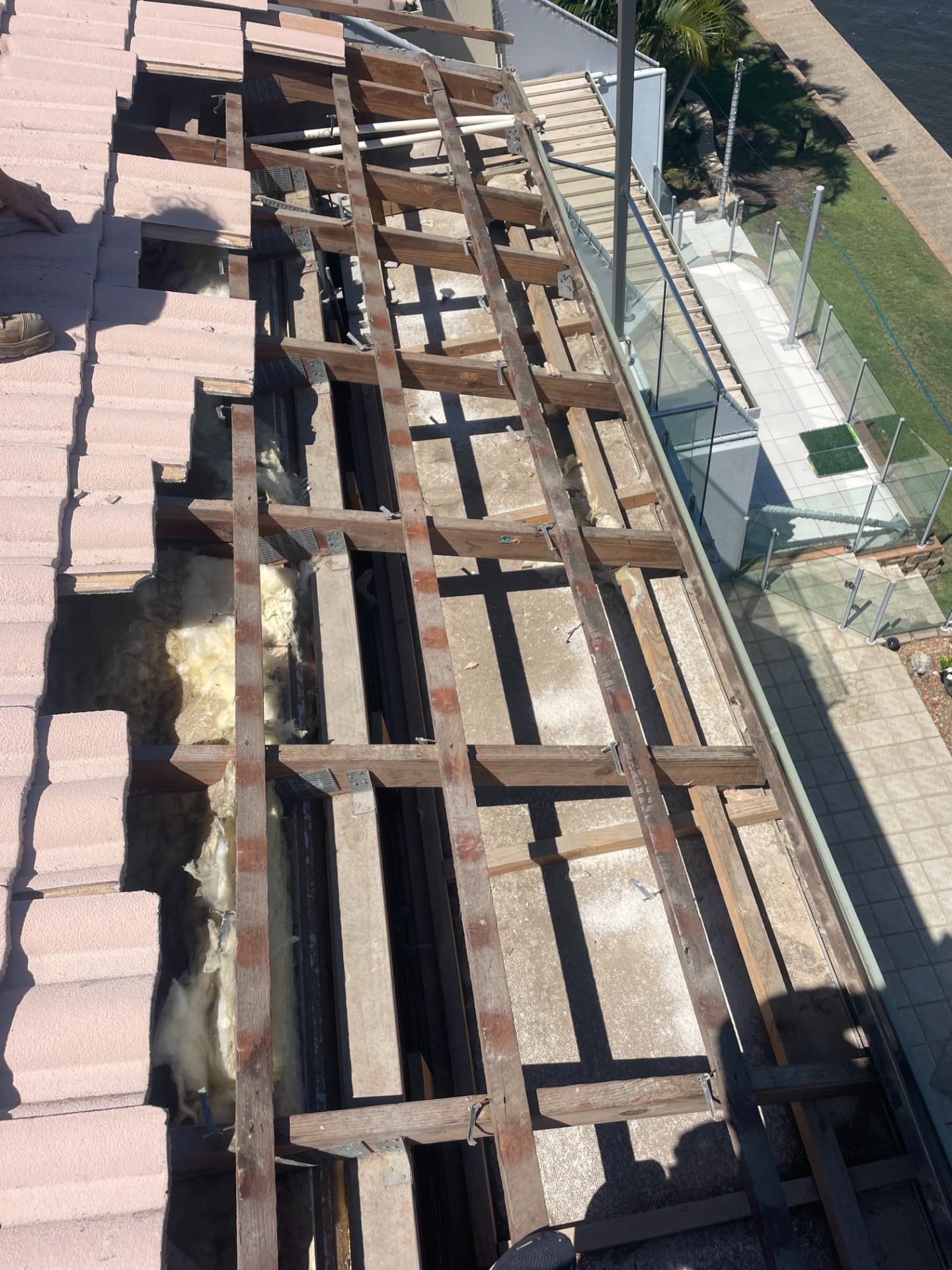 Roof stripped back to timber battens and framing above a glass-balustrade terrace