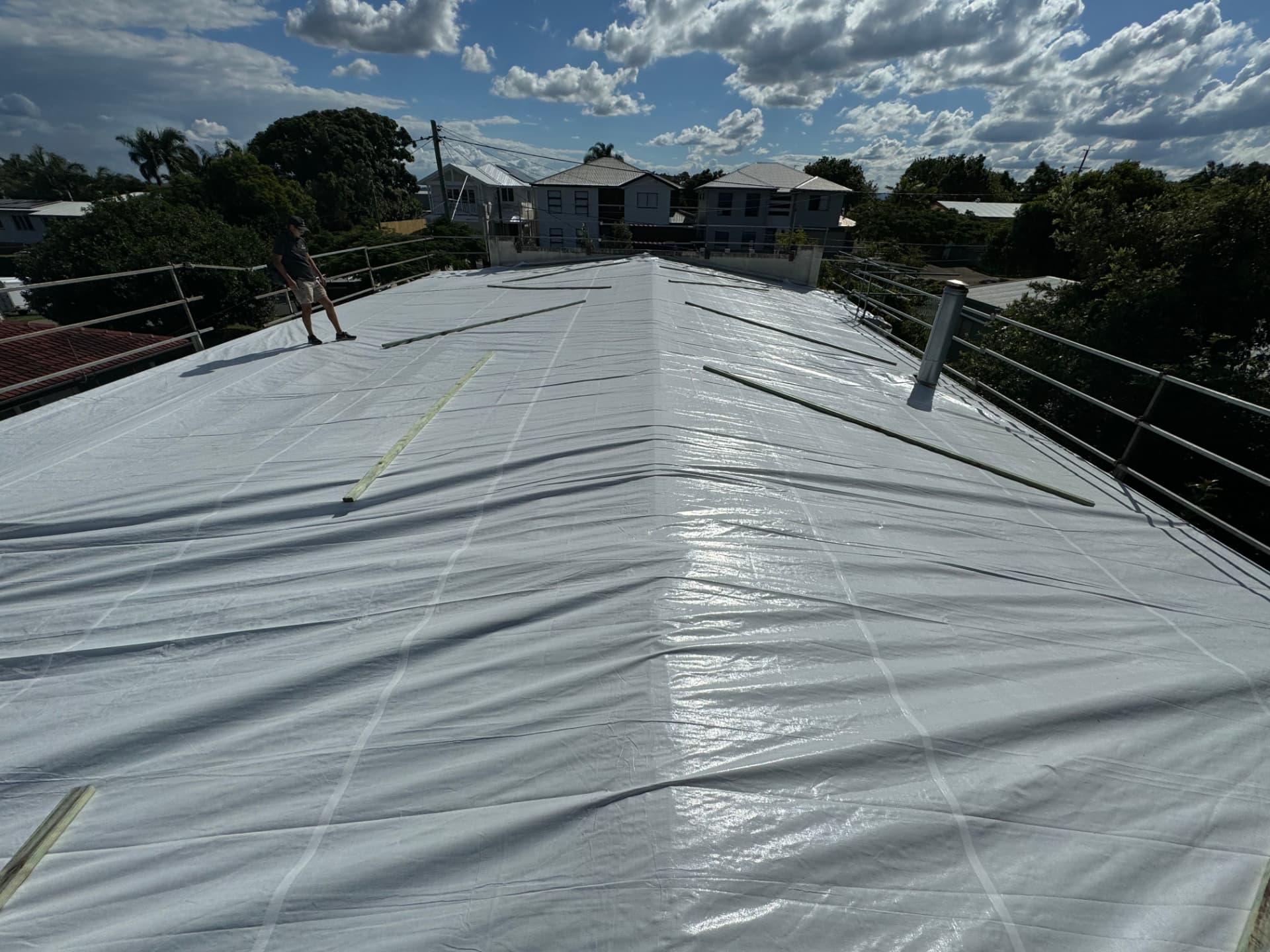 Full roof plane encapsulated in heavy white temporary sheeting, battened down and walked by a team member