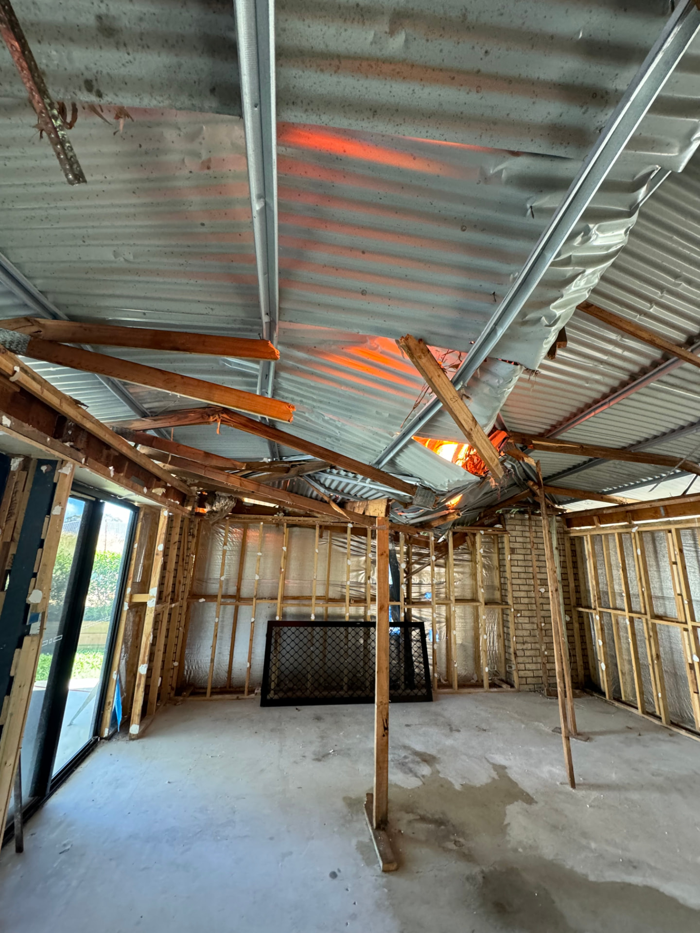 Interior view of a residence with collapsed roof framing and torn sheeting above stripped wall frames