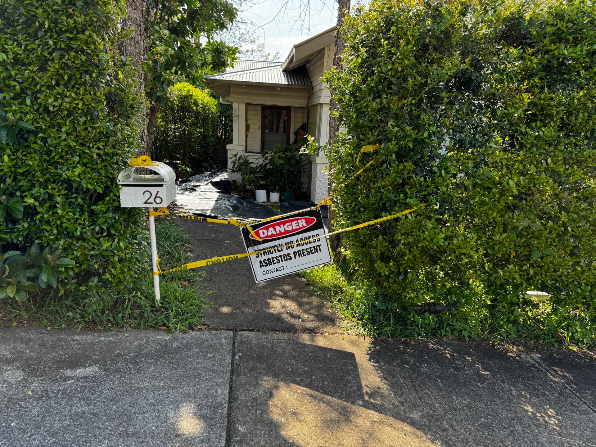 Property entry taped off with hazard tape and a Danger — Asbestos Present sign before works begin