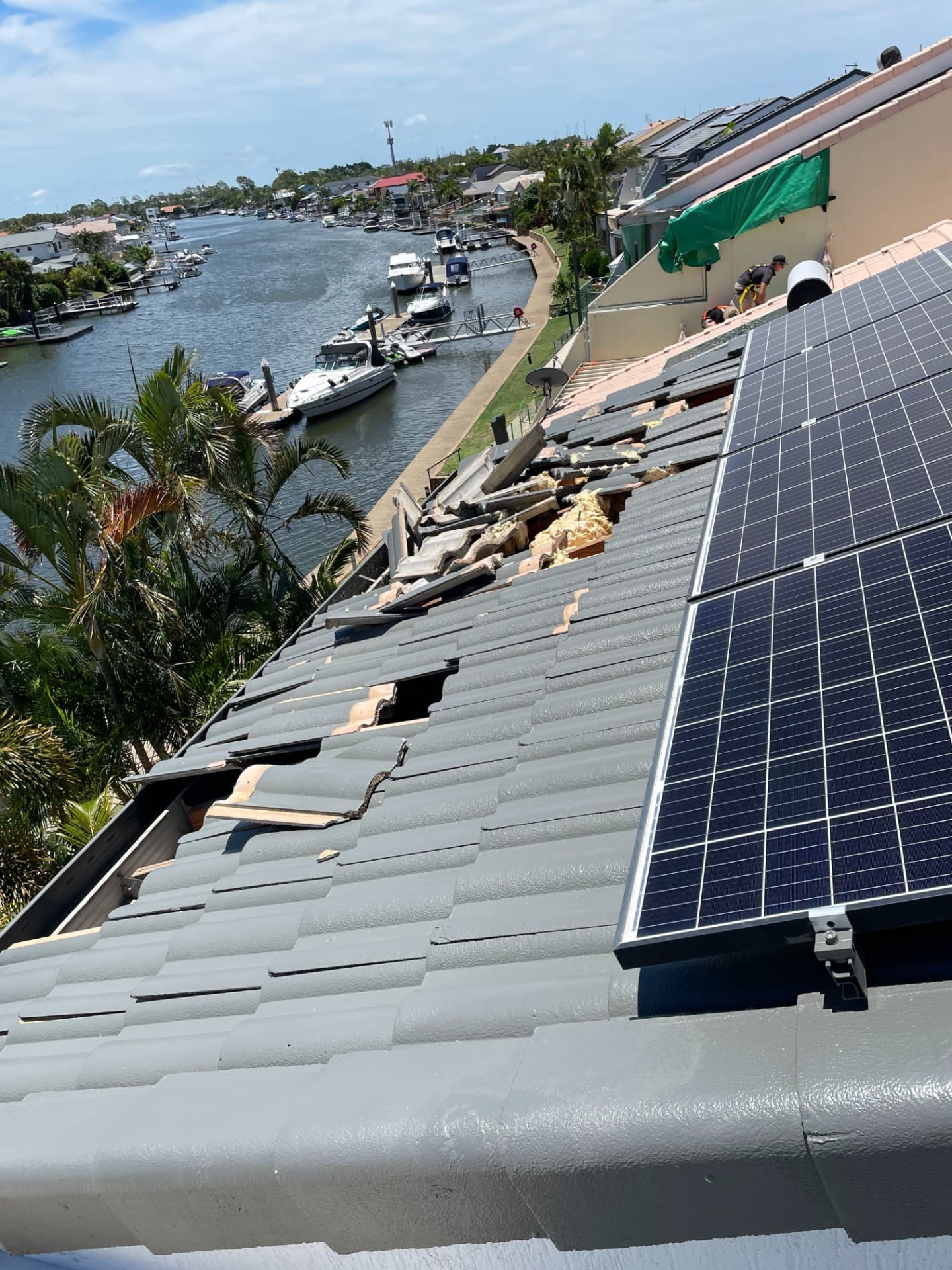 Tiles lifted and displaced along a canal-front roof ridge with a team member working beside the solar array