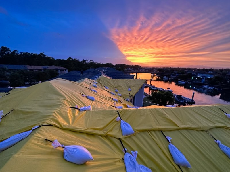 Multiple roof sections sheeted in yellow temporary protection and ballasted at sunrise