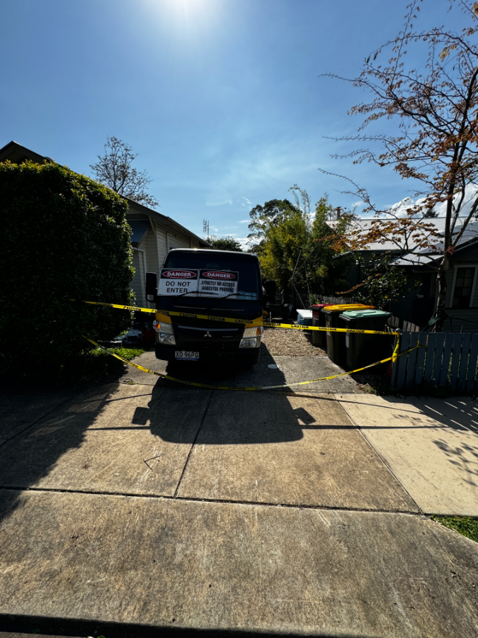 Removal truck signed with Do Not Enter and asbestos warnings inside a taped exclusion zone
