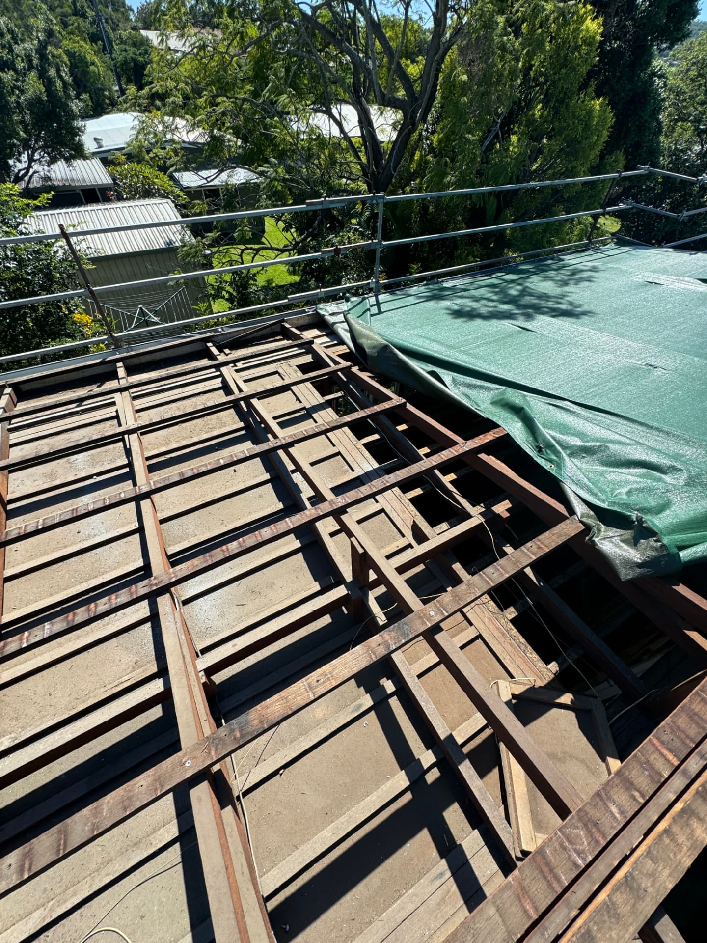 Roof stripped back to timber battens behind edge-protection scaffold, with temporary sheeting over the adjoining section