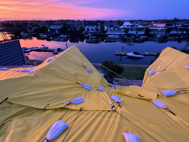 Full roof planes covered in yellow temporary protection above a canal at sunset