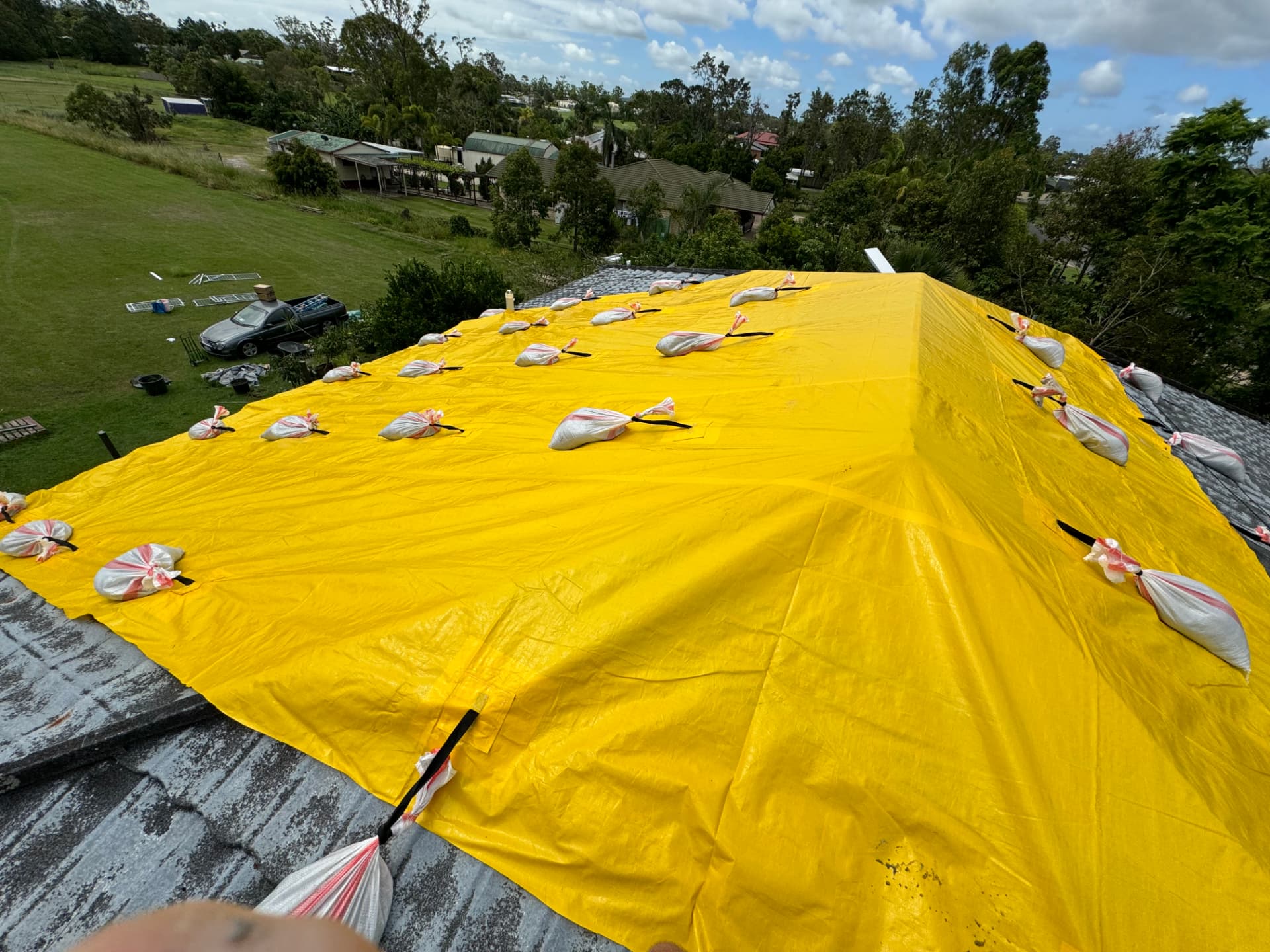 Entire hip roof covered in a single yellow tarp, strapped and sandbagged across every seam
