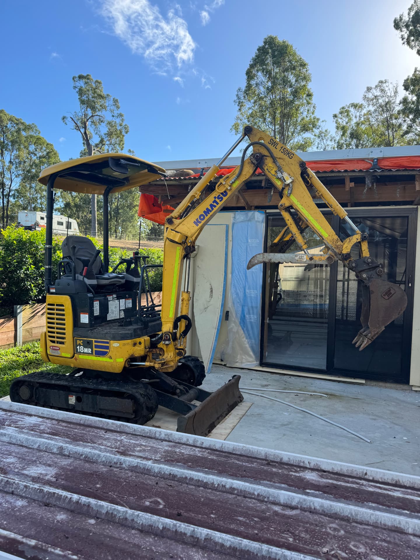 Mini excavator positioned at a damaged residence with temporary sheeting and containment across the opened structure