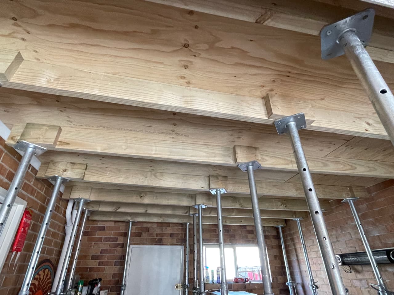 Row of acrow props carrying temporary bearers beneath a plywood-lined ceiling